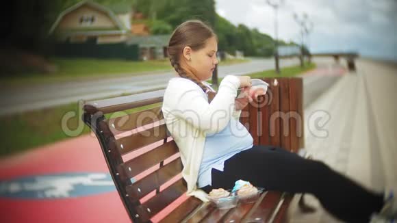 一个可爱的小胖女孩双手坐在公园的长凳上吃蔬菜健康的概念视频的预览图