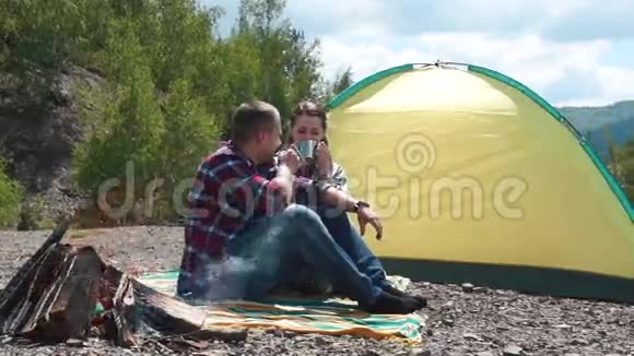 年轻的游客夫妇在营地与篝火在岩石山顶在青山漂亮女孩微笑然后把她视频的预览图