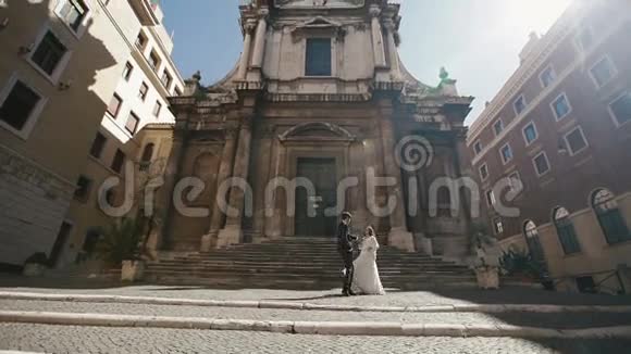 在罗马的婚礼情侣走在圣尼古拉达托伦蒂诺教堂前时髦的新郎轻轻握住他的手视频的预览图
