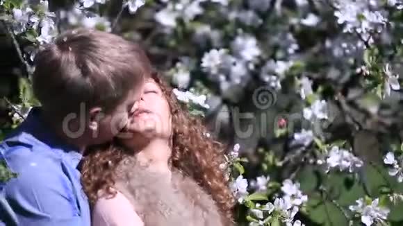在盛开的樱桃园里被喜爱的性感情侣年轻人在树下亲吻他的女朋友视频的预览图