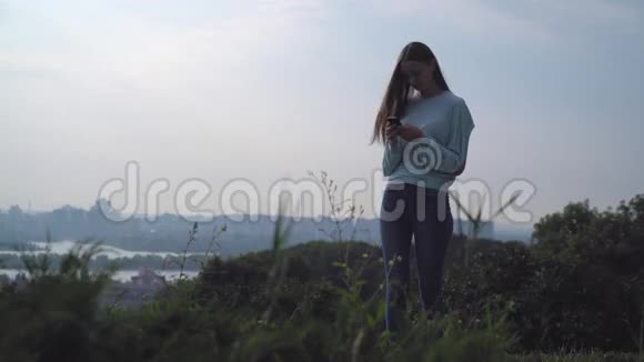 一个年轻女孩站在山上看着你的手机视频的预览图