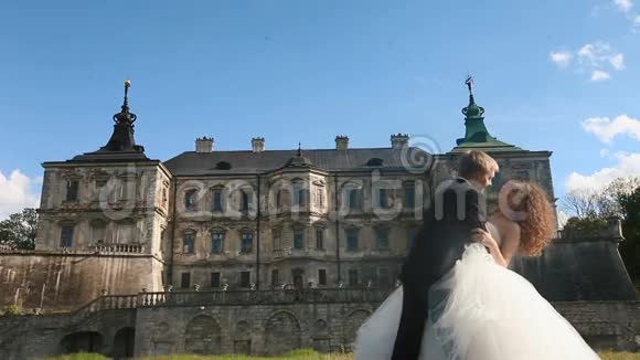 可爱的新郎倾斜他美丽的新娘亲吻她的脖子蓝天下的宏伟古色古香的城堡视频的预览图