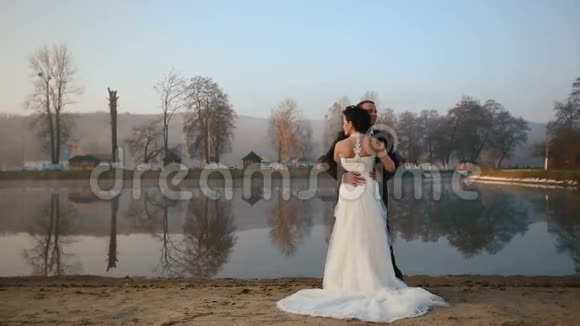 两对新婚夫妇在结婚当天晚上在日落山上度假的湖边拥抱视频的预览图