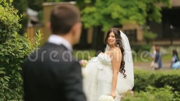 快乐的新婚新郎和新娘在夏季公园嬉戏的新娘召唤她慈爱的新丈夫视频的预览图