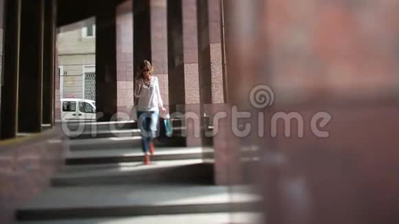 漂亮的女士戴着太阳镜穿着轻便的夏季衬衫和牛仔裤购物后走在靠近花岗岩的楼梯上视频的预览图