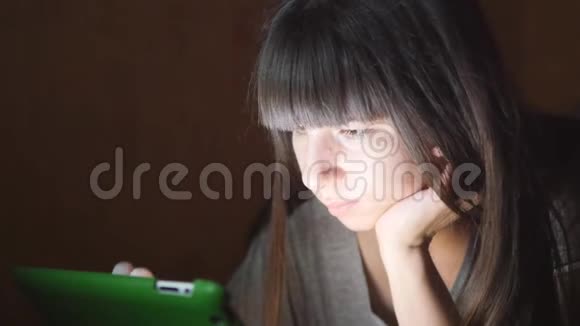 躺在沙发上有平板电脑的年轻女子女孩在家里使用平板电脑深夜在脸上闪耀着光芒视频的预览图