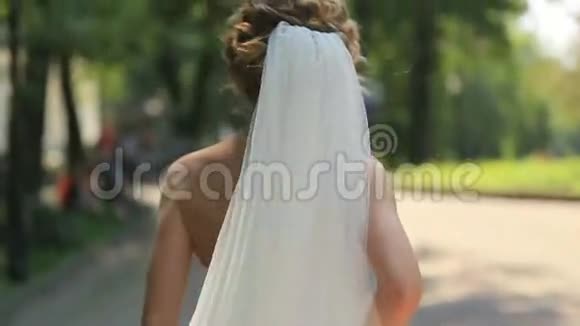 在阳光明媚的小巷里散步时穿着华丽白色礼服戴着长长的面纱快乐地举起双手视频的预览图