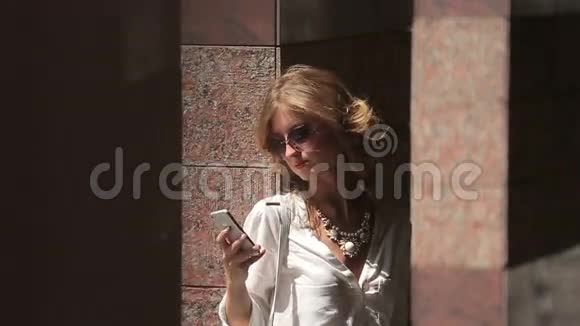漂亮的商务女性带着手机站在现代城市建筑的大理石附近视频的预览图