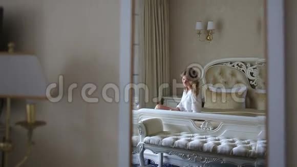 年轻女子早上看书坐在舒适的豪华床上视频的预览图