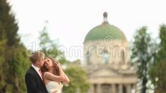 刚结婚的情侣在公园里和远处的古董教堂拥抱在一起视频的预览图