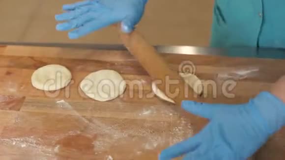 面包店木制桌子上的面包师手拿手套擀面团视频的预览图