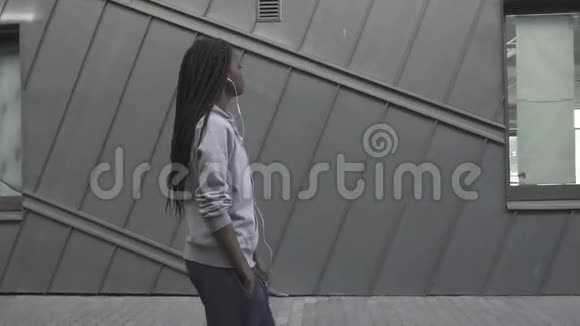 一个有吸引力的非洲裔美国妇女的侧视戴着耳机走路和听音乐灰色纹理视频的预览图