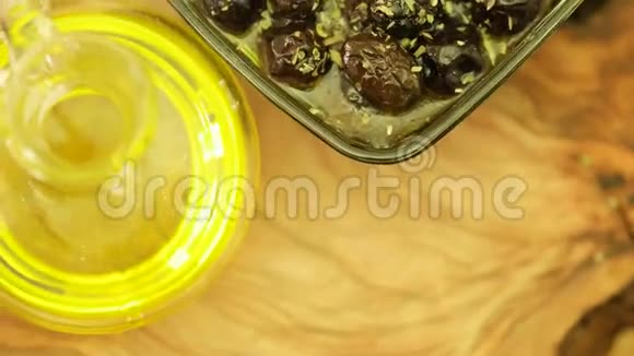 新鲜的百里香叶放在黑色橄榄上自然橄榄油瓶旋转视频的预览图