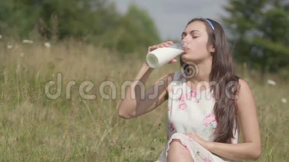 布鲁内特女孩在村里的草地上喝新鲜牛奶视频的预览图