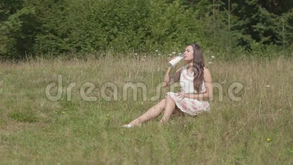 布鲁内特女孩在村里的草地上喝新鲜牛奶视频的预览图