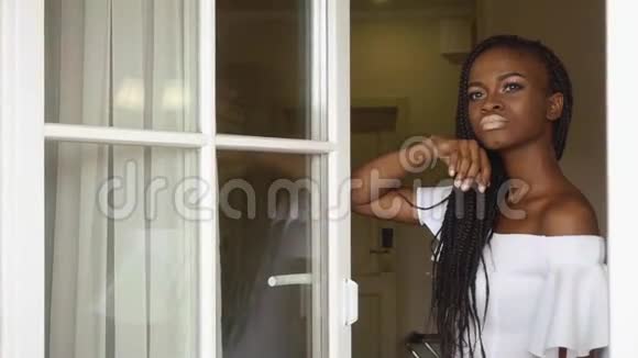 优雅的非裔美国女士体贴地透过窗户看着豪华酒店公寓的背景视频的预览图