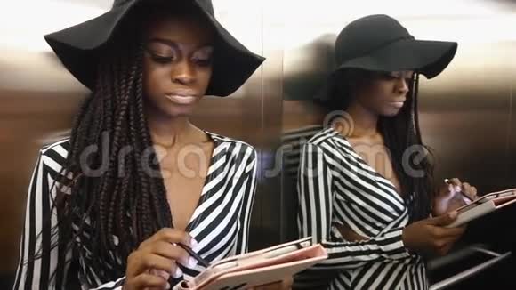穿着条纹鸡尾酒连衣裙的优雅迷人的非洲裔美国女性使用她的平板电脑视频的预览图