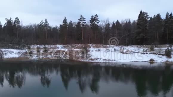 空中观景冬林中的湖泊在多云的冬季天气中飞过一个没有结冰的湖五彩缤纷的风景霜冻的前夜视频的预览图
