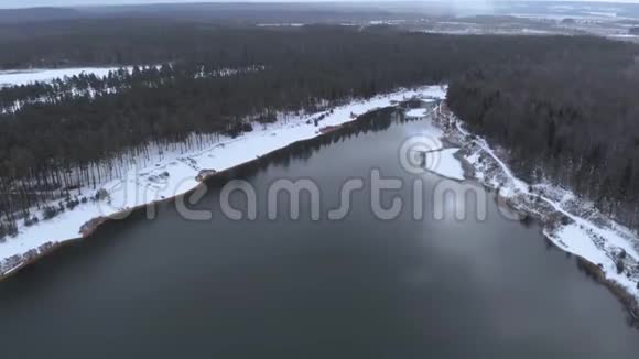 空中观景冬林中的湖泊在多云的冬季天气中飞过一个没有结冰的湖五彩缤纷的风景霜冻的前夜视频的预览图