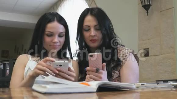 两个女孩在咖啡馆里用手机看照片视频的预览图