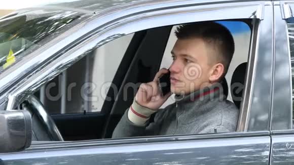 年轻人在路上停车用手机说话开车的商人在智能手机上讲话视频的预览图
