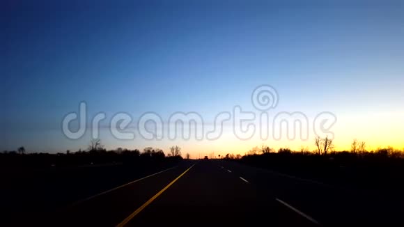 日出时分驱车行驶在乡村公路上黎明时分太阳升起地平线时驾驶员的视角视频的预览图