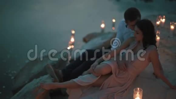 一个英俊的年轻人拥抱着迷人的女孩穿着淡粉色的裙子躺在沙滩上点燃蜡烛视频的预览图