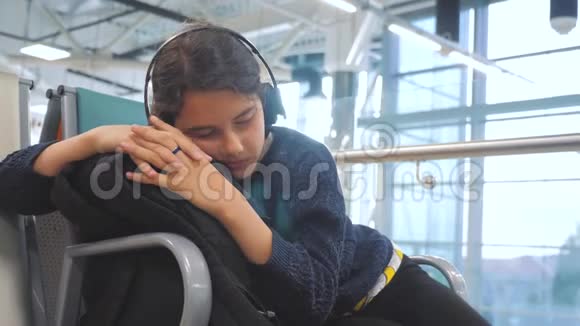 一个戴着耳机的少女睡在机场等着飞机起飞的大门长椅上的旅行者视频的预览图