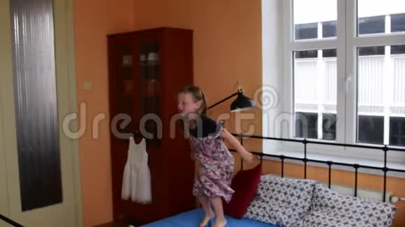 可爱的小女孩在床上跳舞和跳小女孩穿着花裙子童年观念视频的预览图
