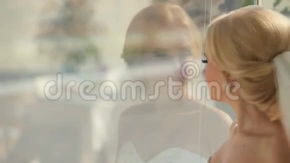 年轻漂亮的新娘透过窗户看着她的新郎走进里面视频的预览图