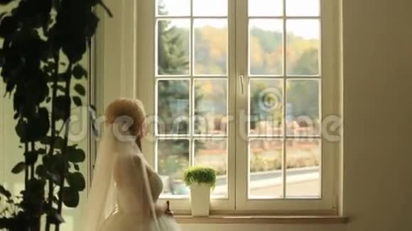 华丽时尚的金发新娘看着窗外在古董房的背景下等待新郎视频的预览图