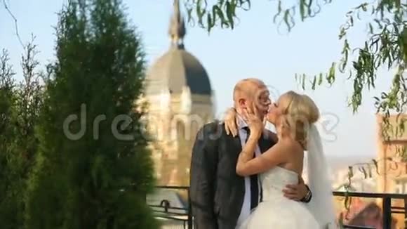 穿着婚纱的美丽新娘和新郎在教堂背景下开心地微笑和亲吻视频的预览图