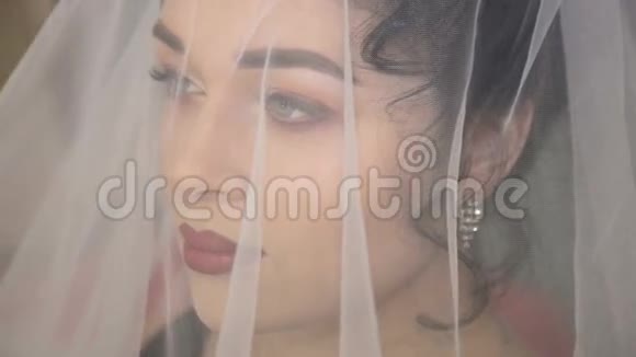 年轻美丽的新娘在白色婚纱下的脸视频的预览图
