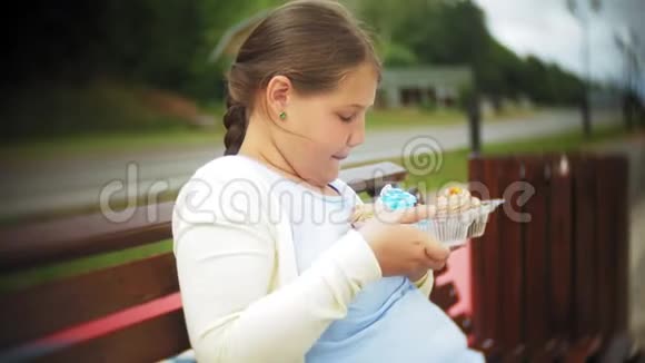 一个可爱的小胖女孩双手坐在公园的长凳上吃蔬菜健康的概念视频的预览图