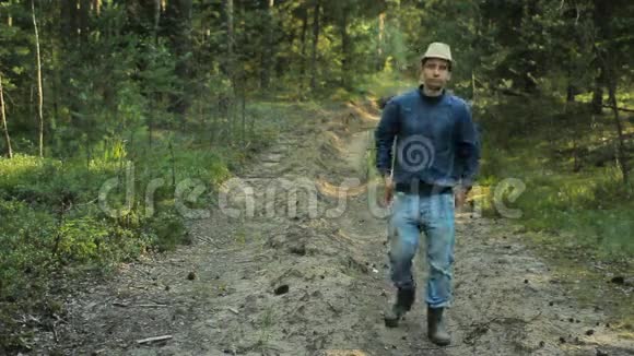 带着帽子在森林里散步的年轻徒步旅行者他调整他的旧牛仔裤继续视频的预览图