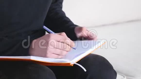 一个英俊的年轻人坐在沙发上在家写笔记本视频的预览图
