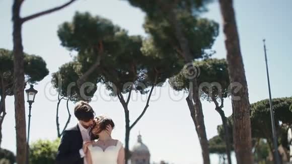 在意大利罗马的公共广场在晴朗的蓝天下举行婚礼时髦的新郎和漂亮的新娘接吻视频的预览图