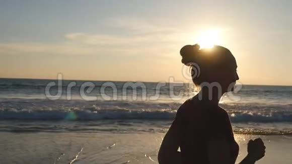 日出时沿着海岸慢跑的女孩日落时在海边奔跑的年轻女子剪影女性视频的预览图
