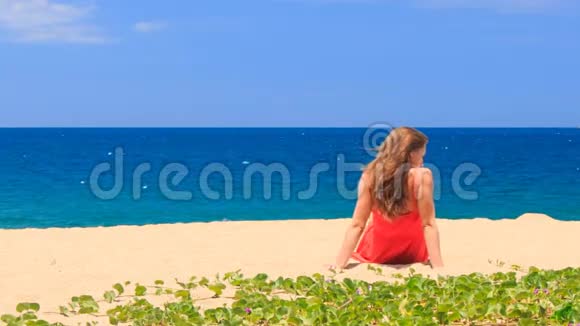 穿红衣服的金发女孩光着脚坐在沙滩上转镜头视频的预览图