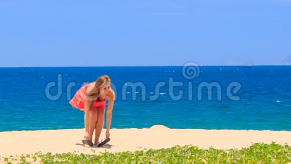 穿红衣服的金发女孩在沙滩上脱掉凉鞋视频的预览图