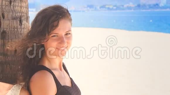 穿着黑色连衣裙的苗条女孩在手掌上说着海滩上的微笑视频的预览图