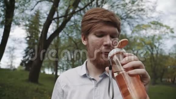 红头发的年轻人有胡子从瓶子里喝水冷饮夏日户外年轻健康人士饮用视频的预览图