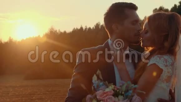 新娘和新郎在夕阳下与绿色草坪在田野里接吻视频的预览图