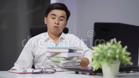 疲惫的学生坐在桌上拿着书和笔记本电脑视频的预览图