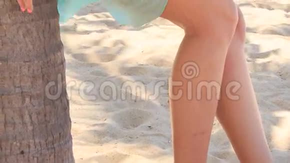 蔚蓝的金发女孩倚在沙滩上的棕榈树干上视频的预览图