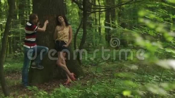 浪漫的爱情时刻年轻漂亮的一对相爱的夫妇在树上刻着他们的首字母春天视频的预览图