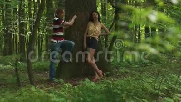 浪漫的爱情故事年轻漂亮的一对相爱的夫妇在树上刻着他们的首字母绿色的春天森林视频的预览图