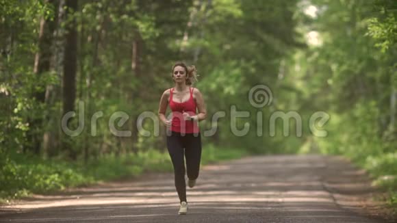 年轻女子在夏天的森林里慢跑这个女孩在大自然中参加运动模型朝相机跑视频的预览图