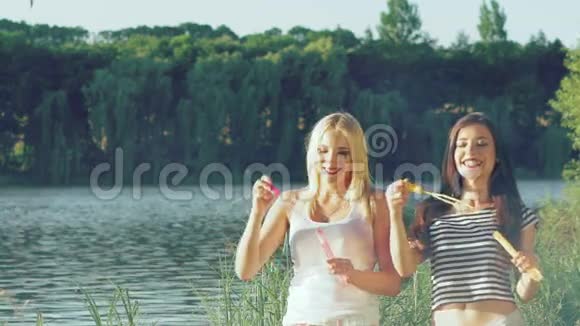 快乐的女孩在湖边吹着五颜六色的肥皂泡慢慢地视频的预览图