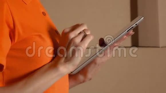 女仓库工作人员穿着橙色制服使用她的平板电脑与棕色纸箱堆叠的背景K4关闭视频的预览图